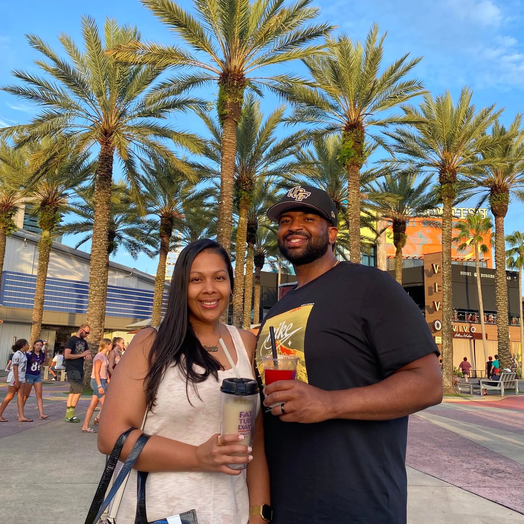 Two people standing together in a palm-lined outdoor shopping area