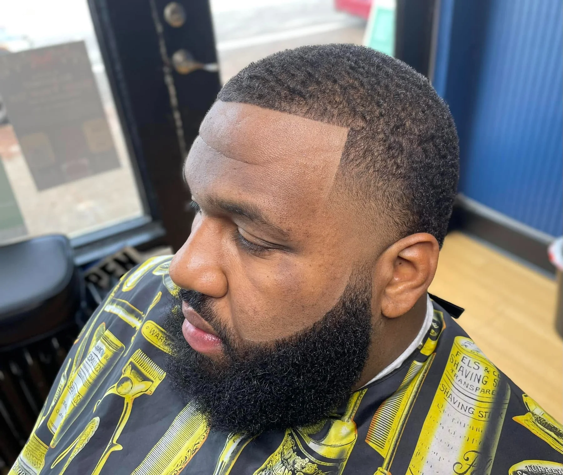 Elevated side view showing a short textured haircut, tapered fade, and outlined beard