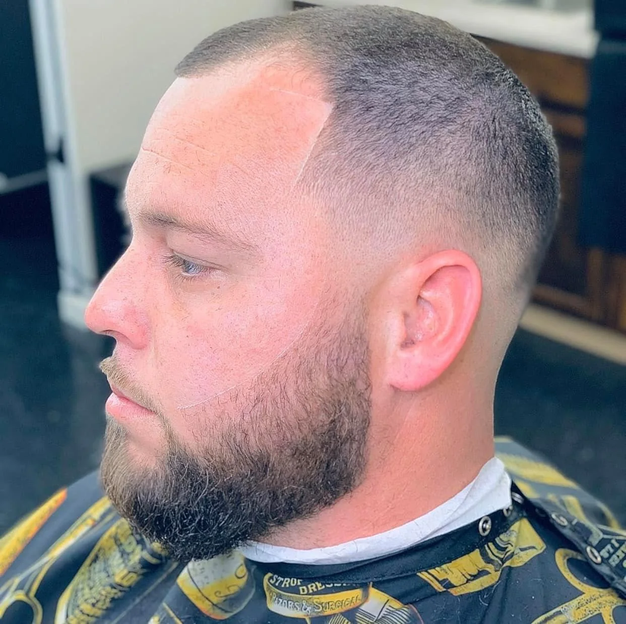 Side profile showing a smooth fade, squared front hairline, and full shaped beard